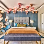 A luxury hotel bedroom styled for romantic getaways Cape Town, featuring a king bed beneath dozens of metallic pink and gold heart-shaped helium balloons.